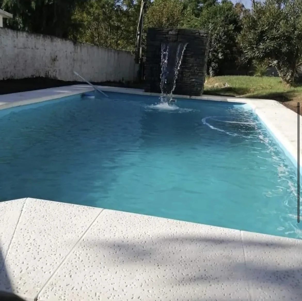 Piscina de agua turquesa con cascada sobre muro de piedra